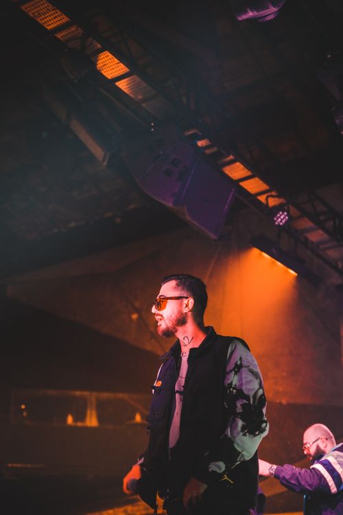 Free Energetic male performer on stage wearing sunglasses, highlighted by vivid lighting and an engaging crowd. Stock Photo