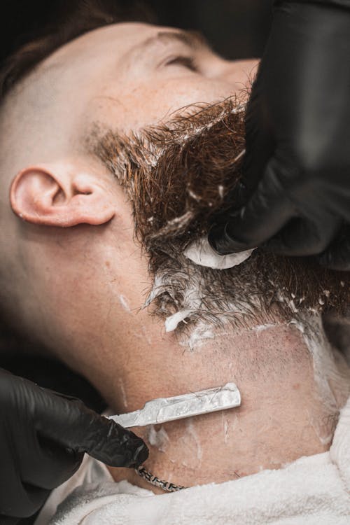 Close-Up Photo of a Person's Hands Shaving a Man's Beard