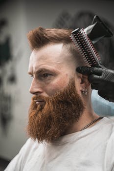 Side view of man with beard getting his hair styled by a barber with a brush.
