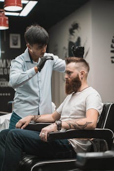 A barber expertly styles a bearded man's hair in a modern barbershop setting.