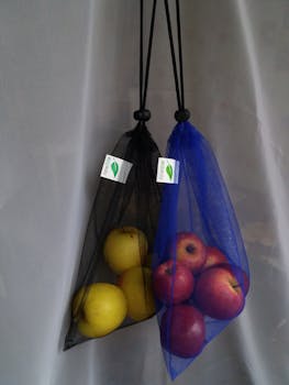 Eco-friendly mesh bags filled with apples and lemons hanging indoors, promoting zero waste.