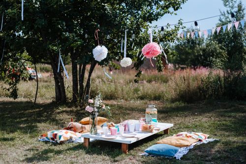 Free A charming outdoor picnic setup with bright decorations and colorful pillows under trees. Stock Photo