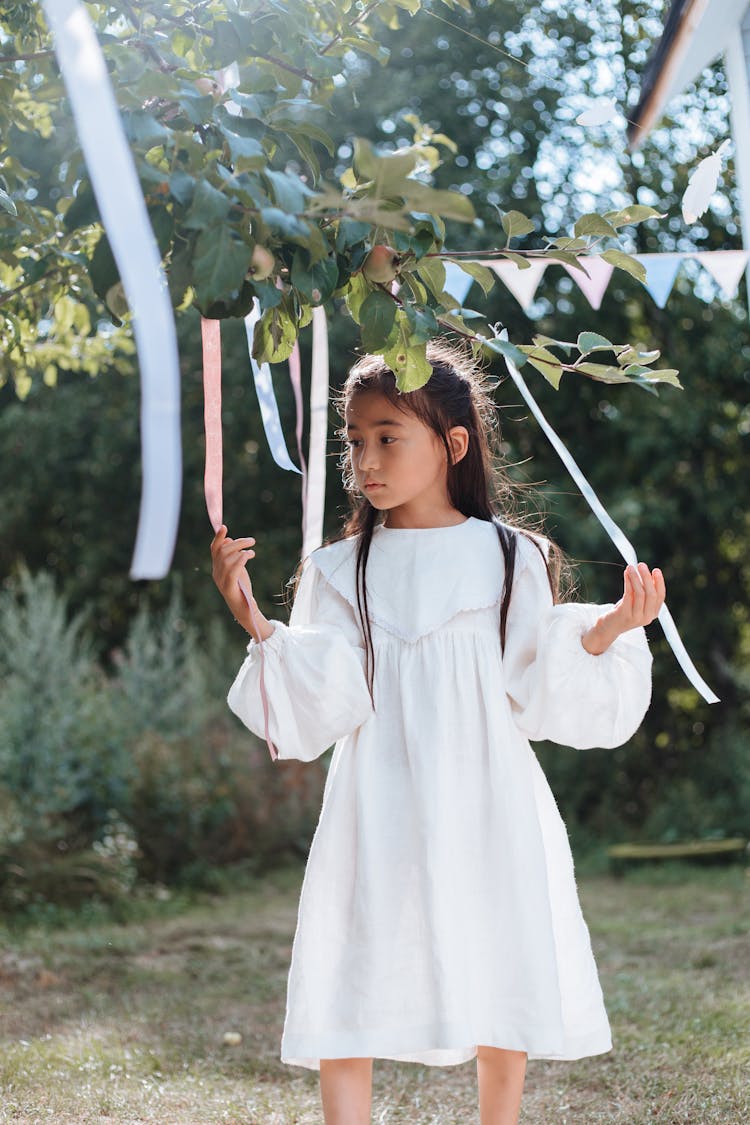 A Girl In A White Dress Holding A Party Decoration