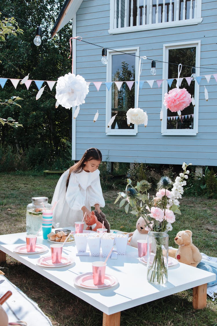 A Girl In White Dress Playing With Stuffed Toys At A Picnic Party