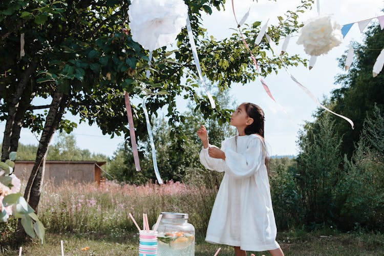 A Girl In A White Dress Looking At A Party Decoration