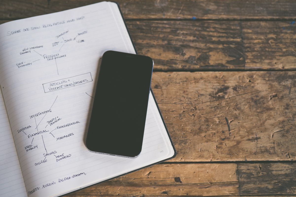 Caiet cu o schema scrisa de mana si un telefon cu ecranul negru, pe lemn brut