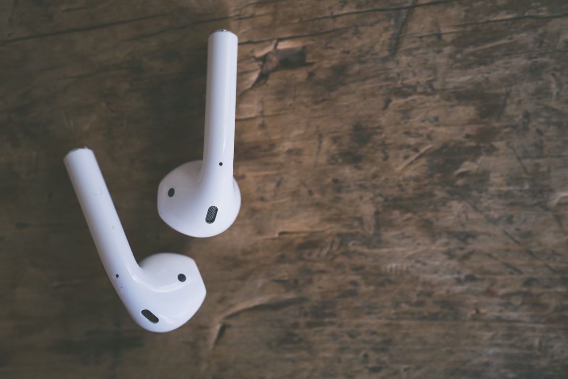 White wireless earbuds resting on a wooden surface, showing the tip and housing design
