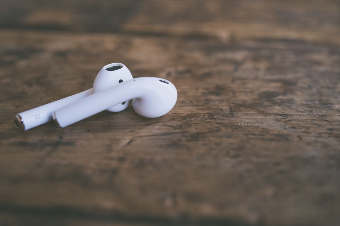 Close-up of white wireless earbuds resting on a wooden table showing the ear tip design