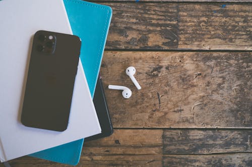 White Airpods Beside Stack of Books with Cellphone on Top