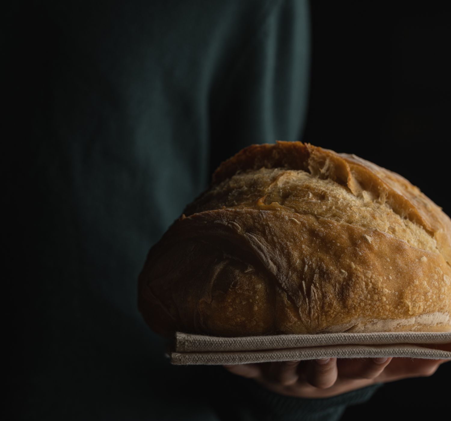 Close-up of a fresh baked loaf of bread held in hands with a dark background.