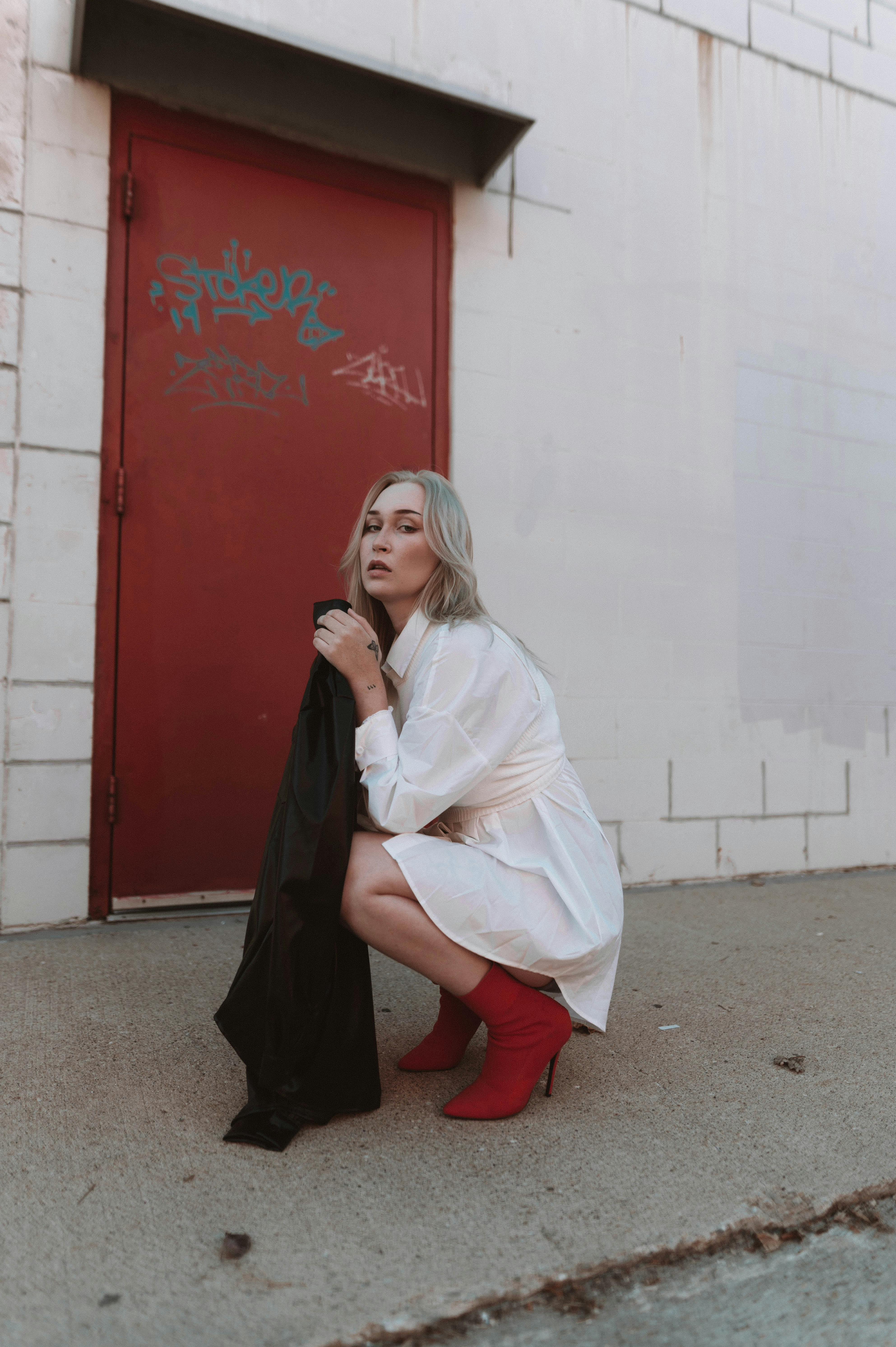 Stylish woman in red high heels crouching in front of a red door against a graffiti wall.