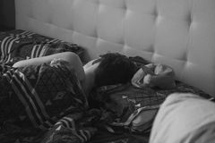 A peaceful black and white photo of a person sleeping in bed with patterned sheets.