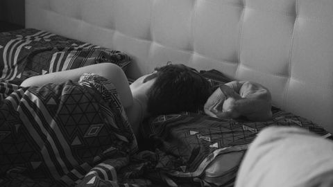 A peaceful black and white photo of a person sleeping in bed with patterned sheets.