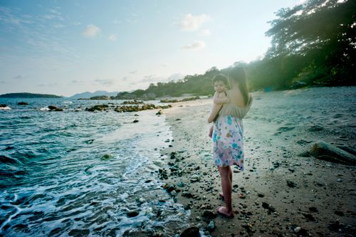 Free A serene moment of a mother holding her child on a secluded beach, capturing the essence of motherhood and nature. Stock Photo