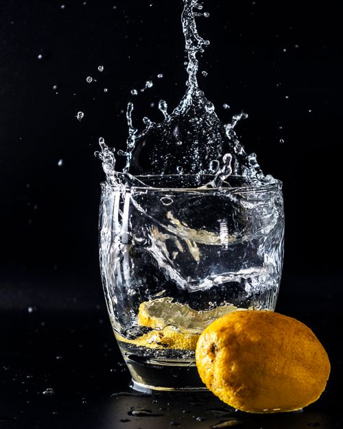Free A dynamic shot of a lemon slice causing a dramatic splash in a glass of water. Stock Photo
