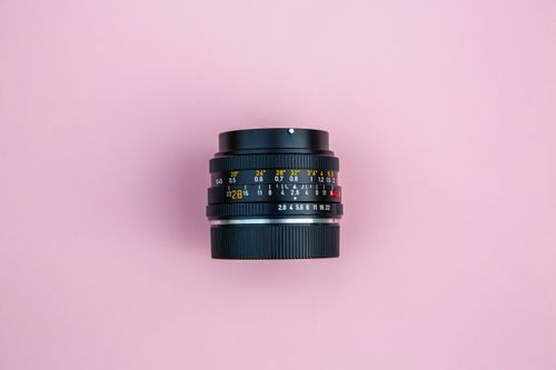 Free Top view of a vintage camera lens isolated on a soft pink backdrop, emphasizing classic photography equipment. Stock Photo