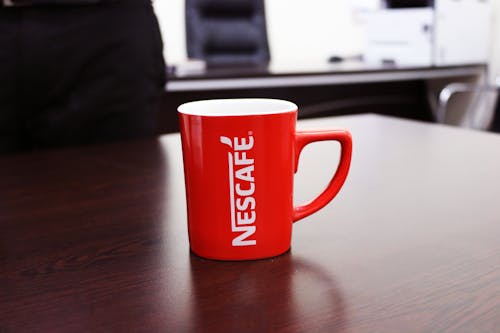 Mug Merah Putih Dengan Motif Nescafe Di Atas Meja Kayu Coklat