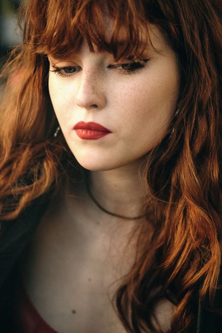 Close-up of a redheaded woman with freckles and red lipstick looking down thoughtfully.