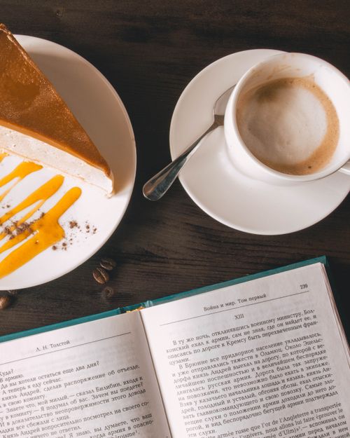 Free Top view of a coffee cup, cheesecake slice, and open book on a wooden table. Stock Photo