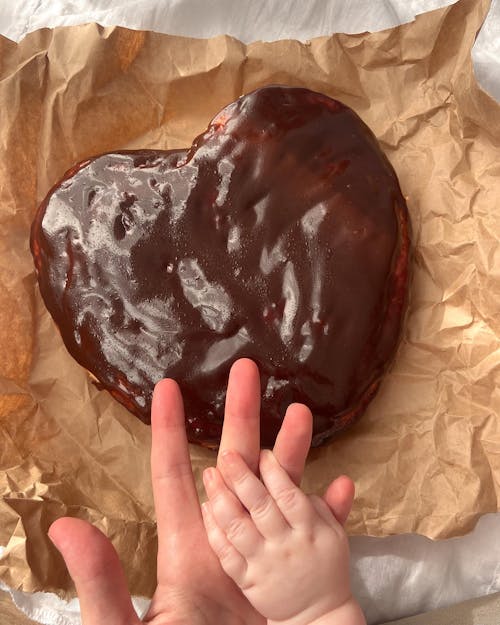 Chocolate Cake in Heart Shape on Creased Baking Paper, and Hands