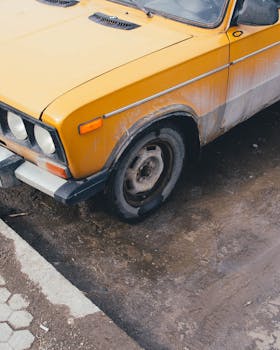 一辆破旧的黄色老式汽车停在泥泞的道路上，镜头给了它一个特写
