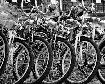 Black and white image of parked vintage bicycles on a street, highlighting spokes and handlebars.
