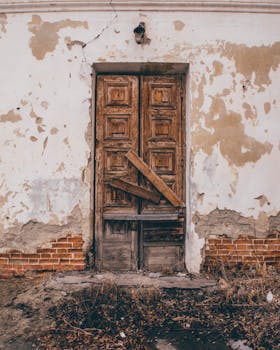 Rustic wooden door on a cracked wall of an abandoned building, showcasing decay and vintage charm.