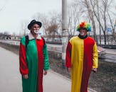 阴天，两个打扮成小丑、穿着色彩缤纷服装的成年人在户外行走