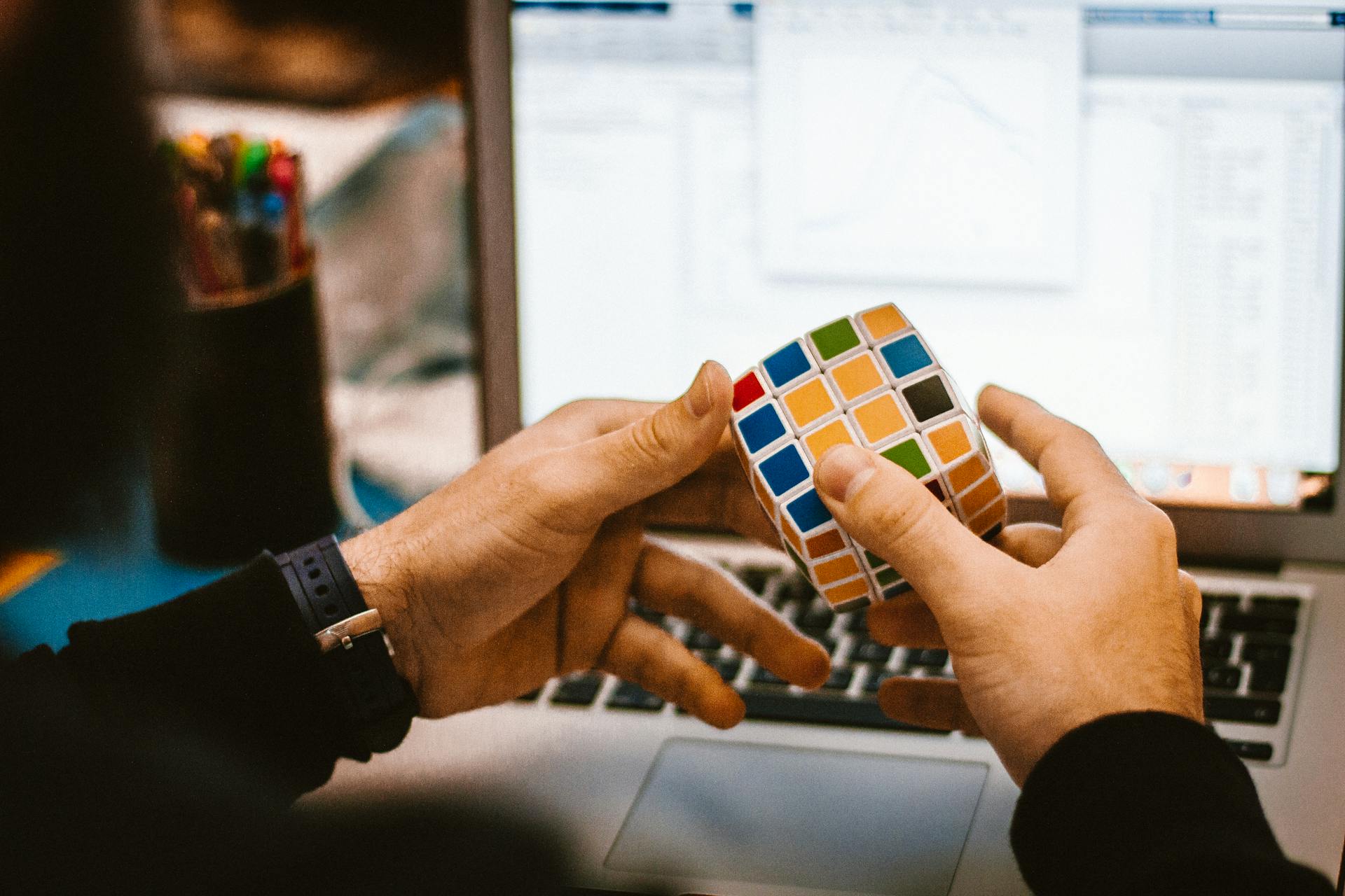 Close-up of hands solving a Rubik's Cube in front of a laptop showcasing a relaxed work environment.