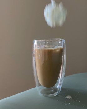 A dynamic view of iced coffee in a clear glass with cream falling into it, creating motion.