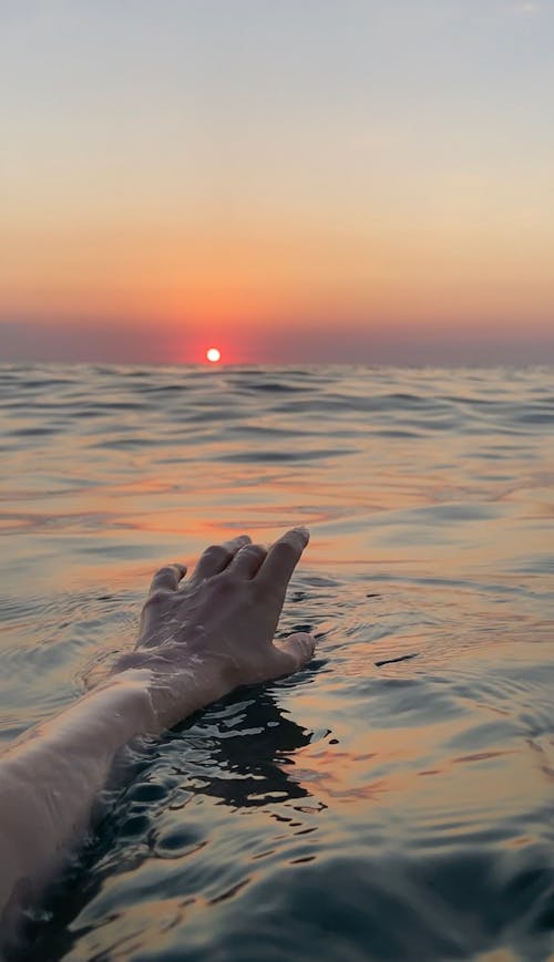 Persons Hand on Water during Sunset
