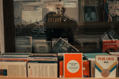 Free A collection of vintage and modern books displayed in a glass shelf, reflecting an antique ambiance. Stock Photo