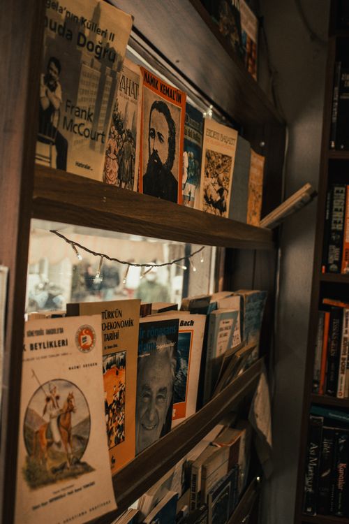 Free A warm-toned bookshelf displaying various books with decorative lights, creating a cozy reading nook atmosphere. Stock Photo