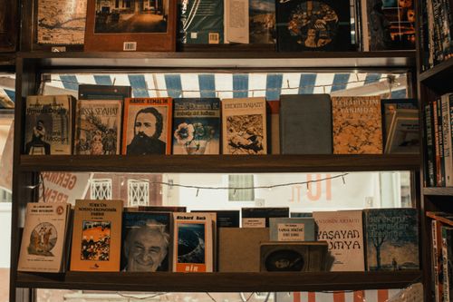Free A cozy bookstore shelf packed with assorted books and string lights in a warm atmosphere. Stock Photo