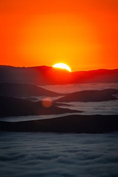 Stunning sunset over mountains with vibrant orange sky and rolling clouds.