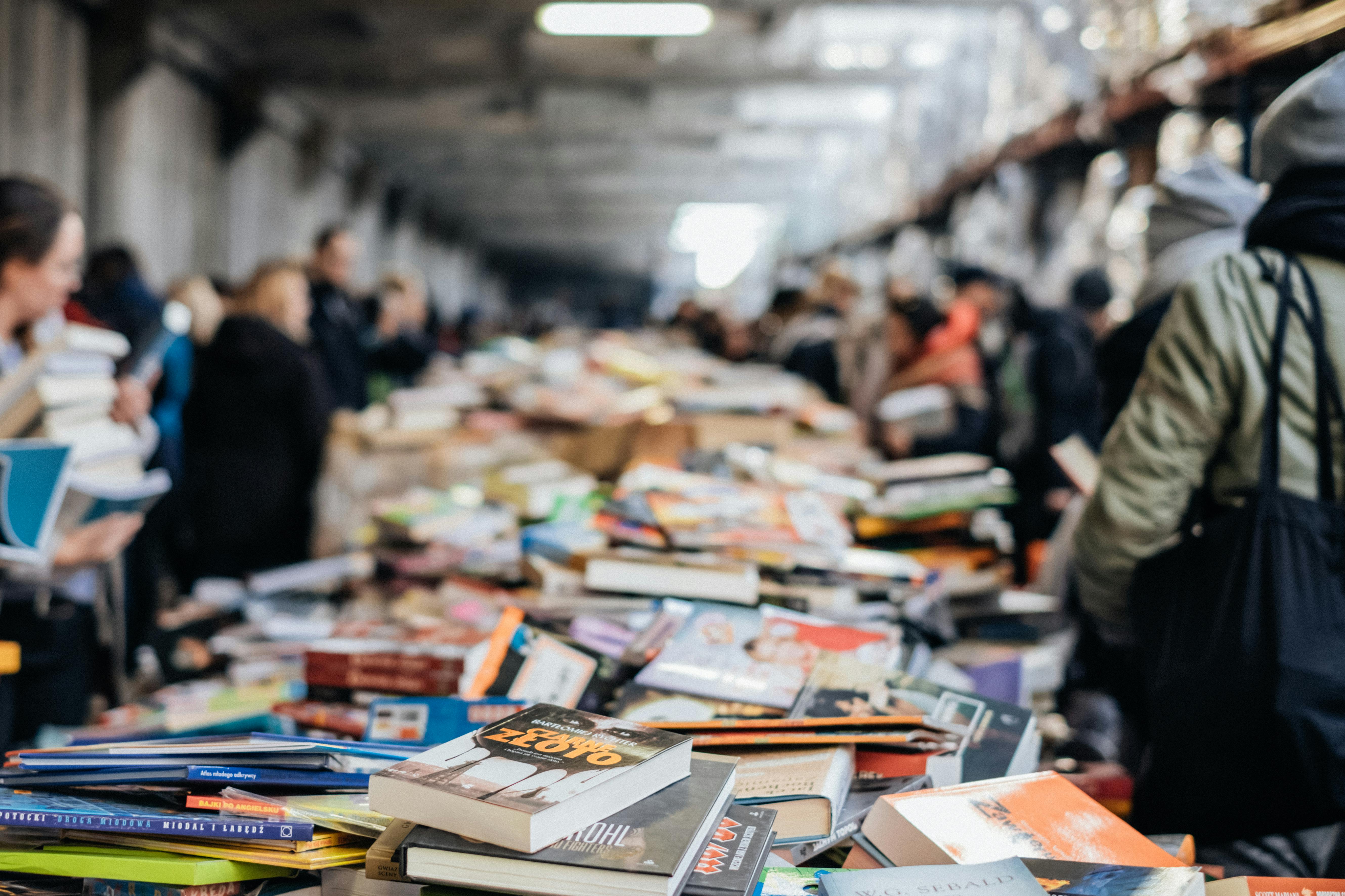 A bustling indoor book sale with numerous books and diverse people browsing.