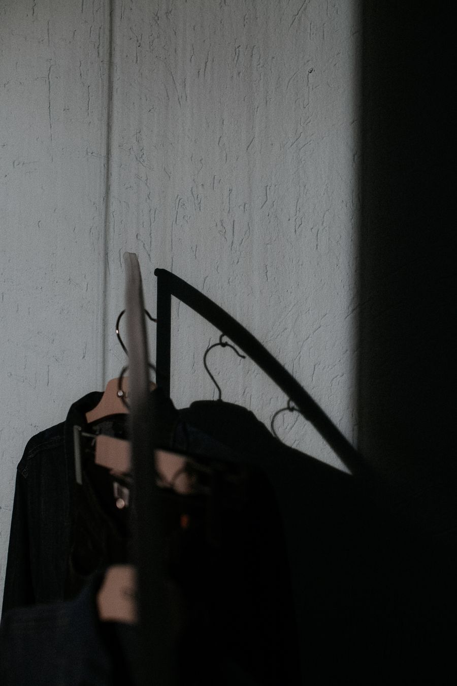 Dark garments on hangers in low raking light — photo by Nikita Nikitin on Pexels