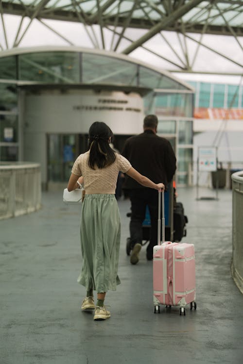 Free Woman in Brown T Shirt Pushing Her Pink Luggage and Man in Black Long Sleeves Pushing Trolley Stock Photo