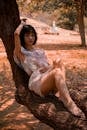 阳光明媚的公园里，一位身穿花卉连衣裙的女子靠在树枝上，营造出悠闲与宁静的氛围