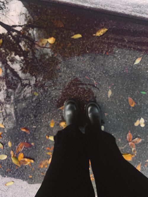 Free Close-up of shoes in a puddle with colorful autumn leaves on wet pavement. Stock Photo