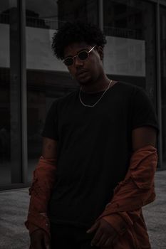 Urban portrait of a fashionable man wearing sunglasses and a necklace, exuding cool style.