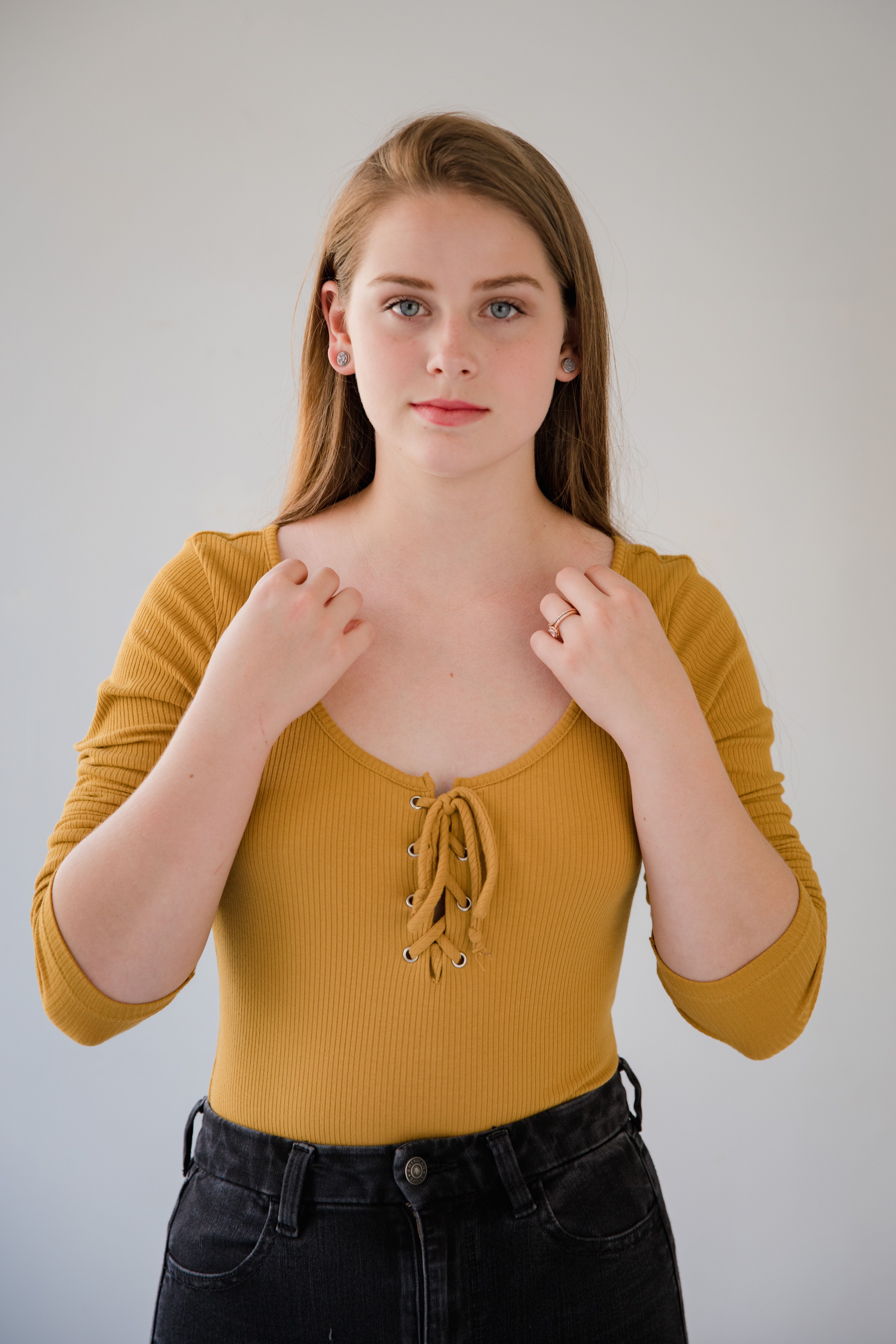 Studio portrait of a young woman in a yellow top, front-facing with a neutral expression.