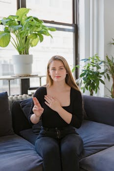 Young woman using sign language on a couch in a bright living room with plants.