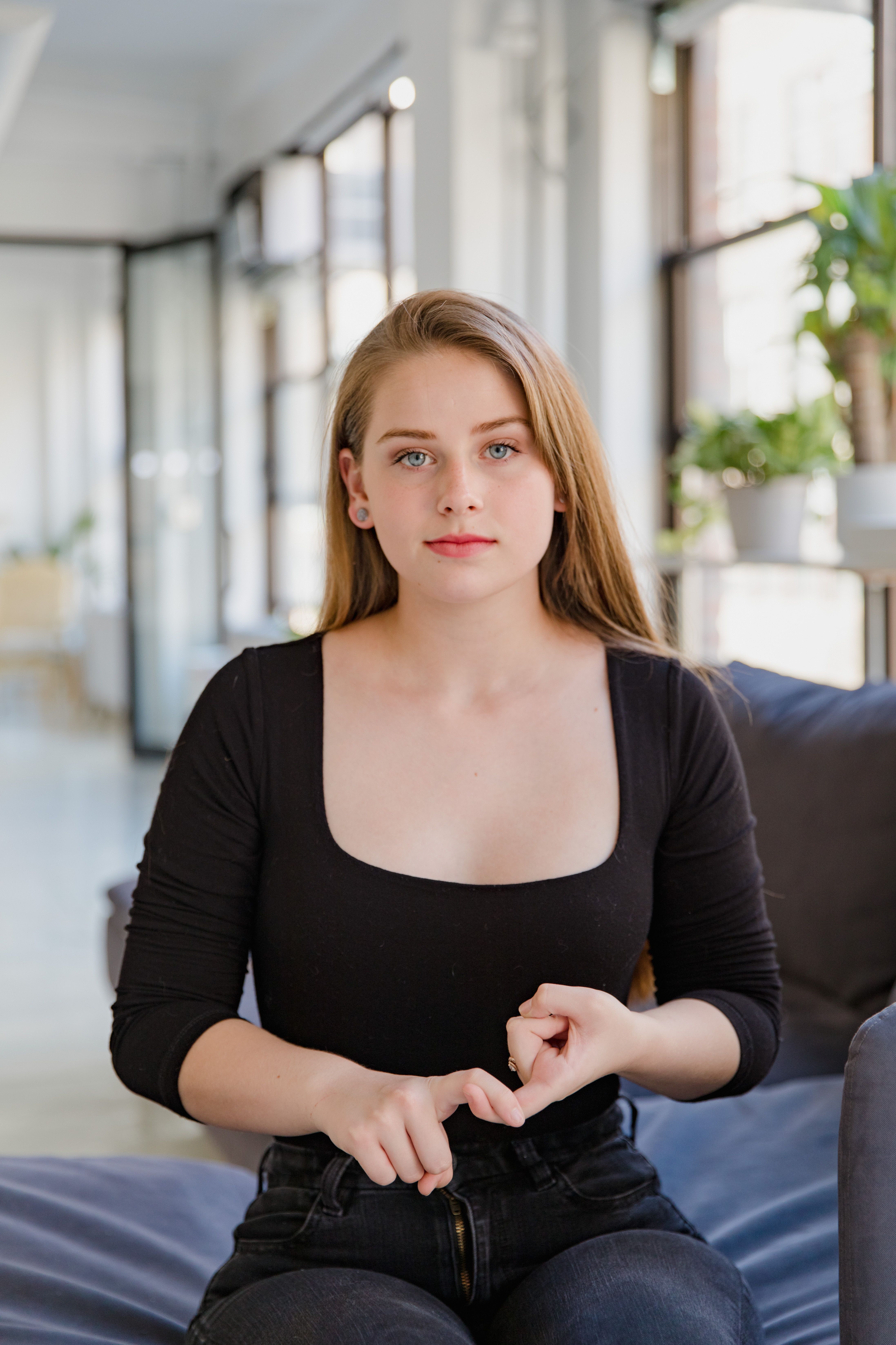 Portrait of a young woman gesturing sign language in a bright living room.