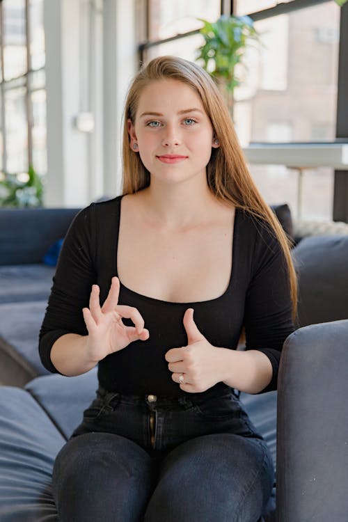 Free Portrait of Smiling Woman Sitting on Sofa, Showing Sign Language Stock Photo