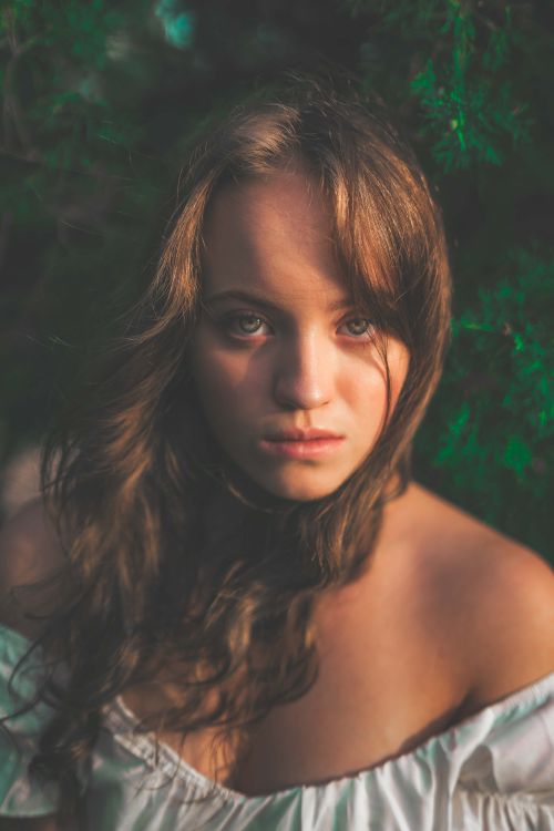 Free Close-up portrait of a young woman with long hair, captured in soft, natural light against a natural background. Stock Photo