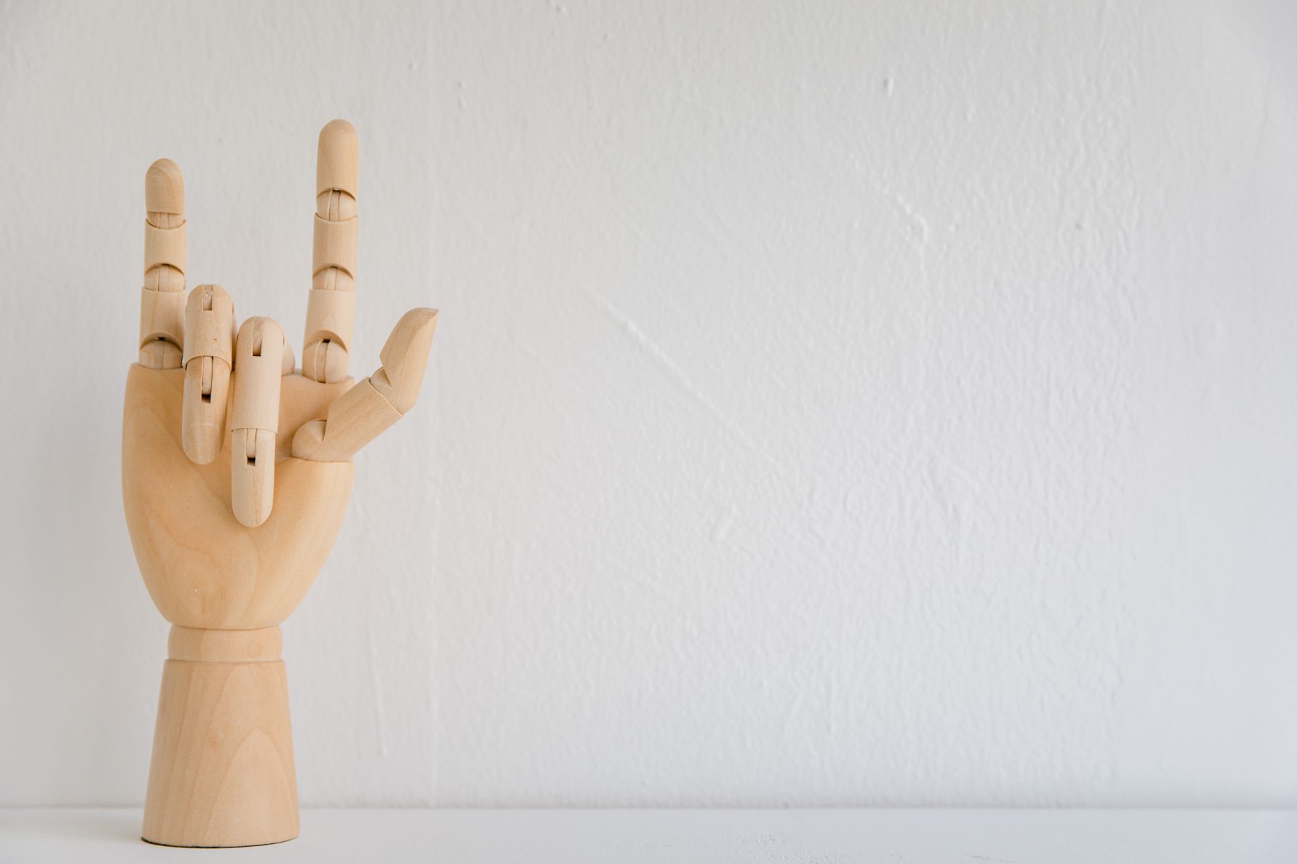Wooden hand model showing a sign language symbol on a white background with copy space.
