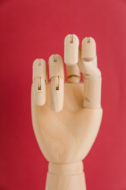Free Wooden mannequin hand posed against a vibrant red background in a studio shot. Stock Photo