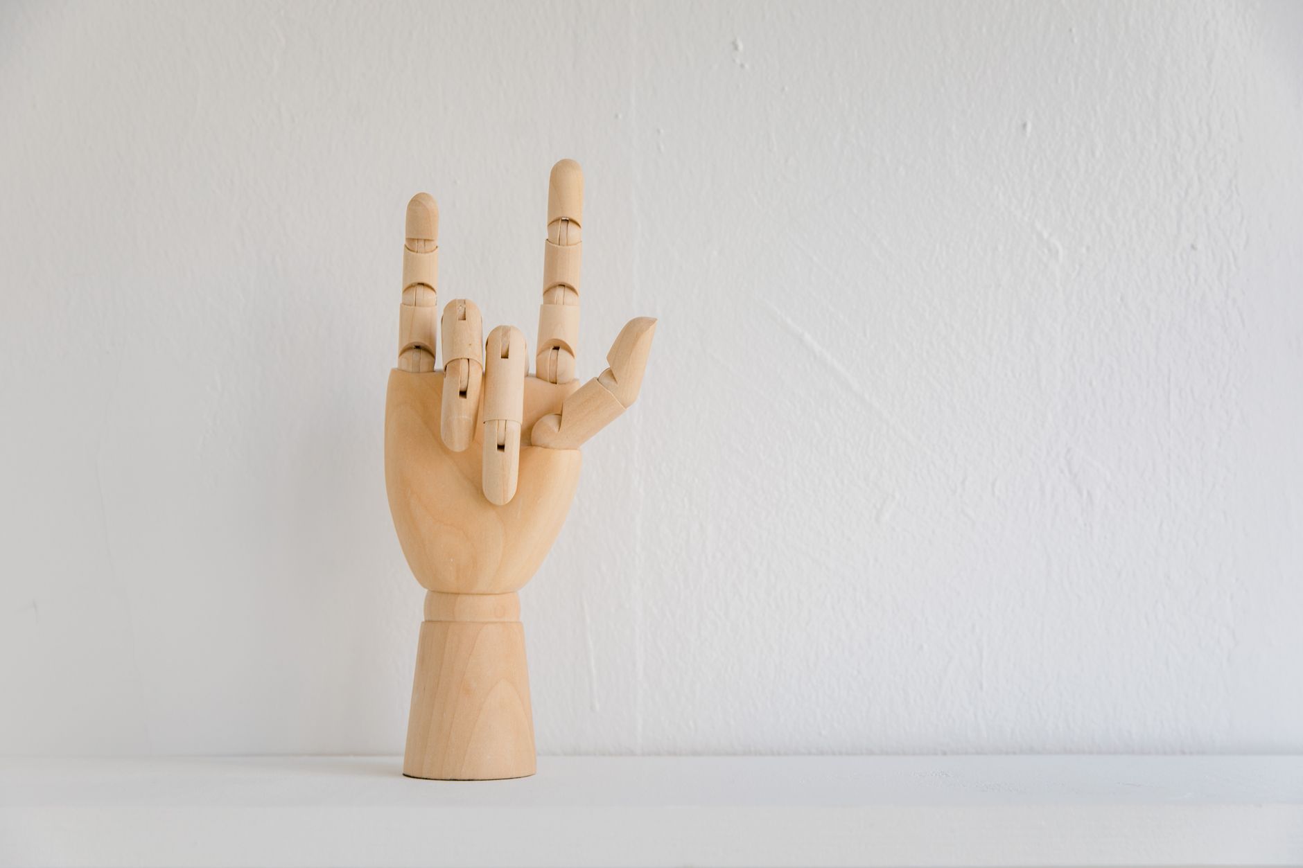 Wooden hand model showing 'I Love You' in sign language on white background.