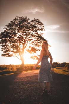 Silhouette of a woman walking on a rural road during sunset with tree backdrop.